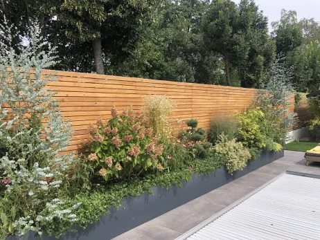 Plantation d'arbustes et vivaces dans un Bac thermolaqué le long d'une clôture en claire voie 